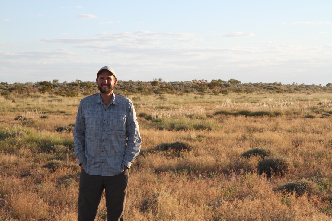 Aaron Wirsing standing among small plants in Australian outback